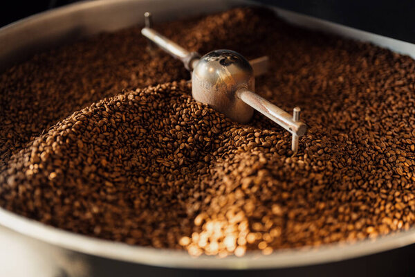 Высокий угол ароматических свежеобжаренных кофейных зерен в большом подносе для охлаждения обжига машины на заводе