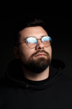 Gözlüklü, kapüşonlu, siyah arka planlı, ciddi, sakallı bir hippi.
