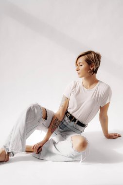 Beyaz arka planda dinlenirken yerde oturan çıplak ayaklı genç bir kadın vücudu.