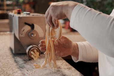 Anonim kadın aşçı mutfakta mermer tezgahta geleneksel İtalyan rulo taze tagliatelle makarna hazırlıyor.