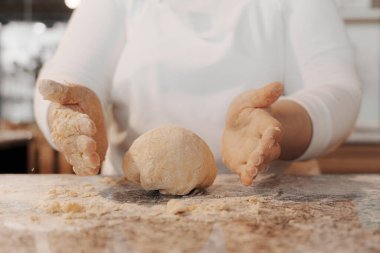 Beyaz üniformalı, hamuru yoğurup mermer tezgahta top yapan isimsiz bir kadın aşçı.