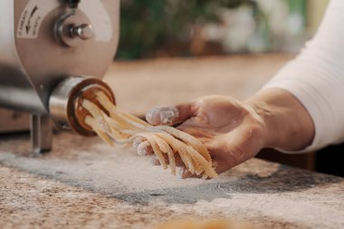 Anonim kadın aşçı mutfakta geleneksel yemek pişirirken hamurdan İtalyan makarnası hazırlıyor.