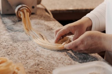 Anonim kadın aşçı mutfakta mermer tezgahta geleneksel İtalyan rulo taze tagliatelle makarna hazırlıyor.