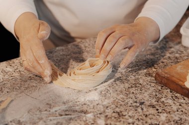 Anonim kadın aşçı mutfakta mermer tezgahta geleneksel İtalyan rulo taze tagliatelle makarna hazırlıyor.