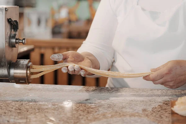 Beyaz önlüklü isimsiz kadın aşçı restoran mutfağında makarna makineli İtalyan tagliatelle hazırlıyor.