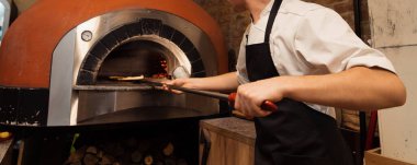 Pizza konsepti. Geleneksel İtalyan pizzasını hazırlıyorum. Pizza için uzun kürek, profesyonel bir fırında hamur pişirmek modern restoran mutfağının içinde ateş yakmak. Yüksek kalite fotoğraf