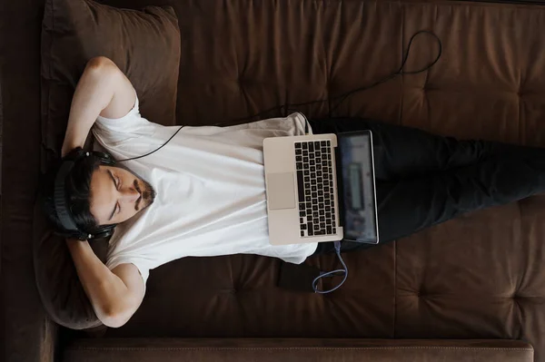 티셔츠와 헤드폰을 음악가가 소파에 노트북에서 음악을 — 스톡 사진