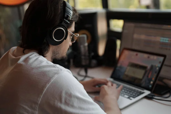 스튜디오에서 캐스트를 티셔츠를 헤드폰을 노트북으로 타이핑하는 집중력있는 음악가의 — 스톡 사진