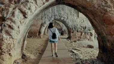 Kız turist antik taş tersanesinde yürüyor. Taş kemerler ve duvarlar. Yüksek kalite 4k görüntü