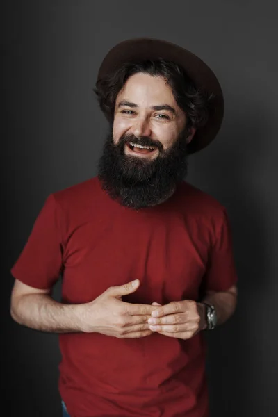 黒を背景に髭を生やしたハンサムなスタイリッシュな男 黒の帽子と赤のTシャツを着た笑顔の男 — ストック写真