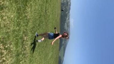 Önünde dağlarla sahada koşan genç bir kadın. Dikey video