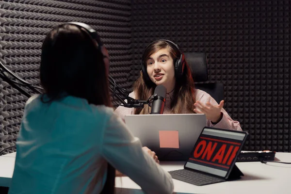 Radio host speaking with guest. Young woman with headphones talking with guest during radio broadcast in recording studio
