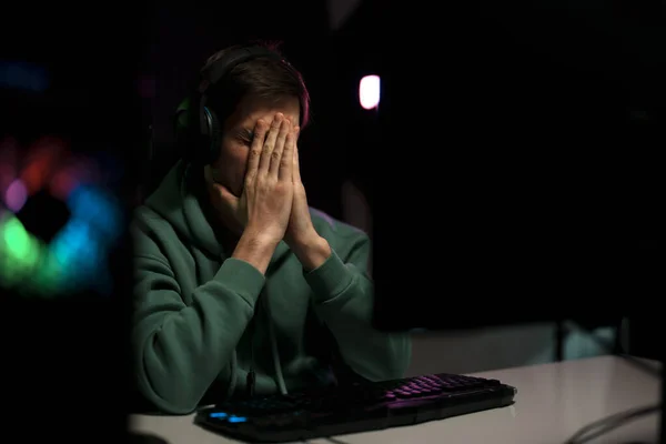 若い失望男性サイバースポーツゲーマーは コンピュータ上でビデオゲームをプレイしながら 祈りの手でテーブルに座って — ストック写真
