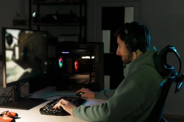 暗い部屋でオンラインビデオゲーム中に競争を持っている間 コンピュータを使用して男性のサイバースポーツゲーマーの側面図 — ストック写真
