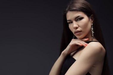 Uzun siyah saçlı, çenesine dokunan ve stüdyoda siyah arka planda kameraya bakan şehvetli genç bir kadın.