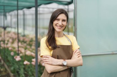 Smiling florist businesswoman portrait wearing yellow t-shirt and brown apron holding arms crossed at the green house