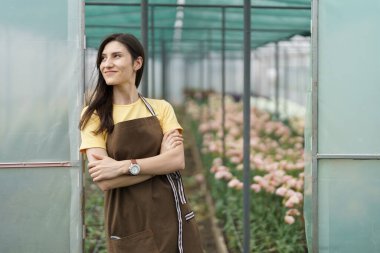 Smiling florist businesswoman portrait wearing yellow t-shirt and brown apron holding arms crossed at the green house