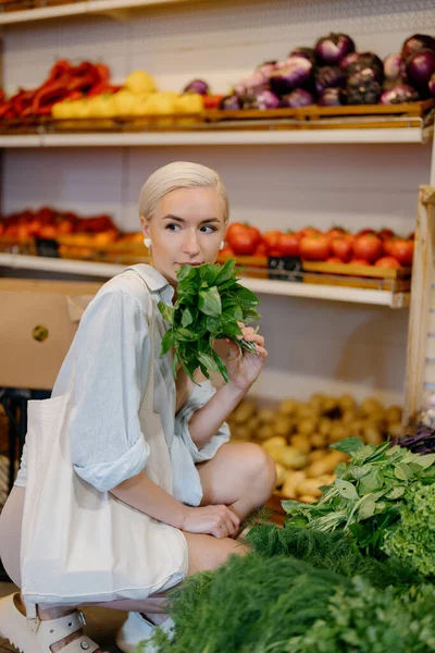 野菜店でさまざまな緑をブラウジングしている女性 彼女はハーブを手に持っている この写真は健康的な食習慣や食料品の買い物の例示に使用することができます — ストック写真