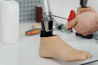 Yakın çekim mahsulü tanınmayan usta, modern protez bacağın metal parçasını tornavida atölyesinde vidalayıp sıkıyor.