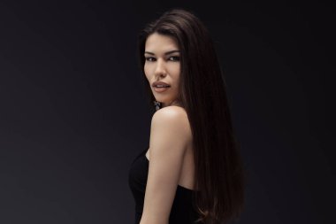 Siyah elbiseli sofistike bir kadın, kendine güveni tam, uzun dalgalı saçları ve ince bir makyajı var.