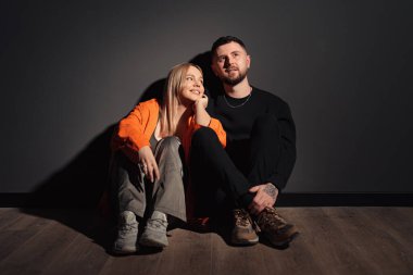 Mutlu bir çift yerde oturuyor, rahat bir şekilde gülümsüyor, yumuşak bir ışık havayı canlandırıyor.