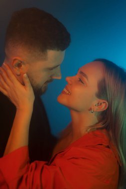 Yüzleri çarpıcı bir neon ışığıyla aydınlanan hassas bir çift anı. Sıcak ve serin ışık, sevgi dolu bakışlarının etrafında samimi bir atmosfer yaratır.