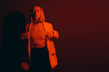 Şık ceketli dengeli bir kadın büyüleyici kırmızı bir ambiyansa karşı modern moda anlayışı sergiliyor.