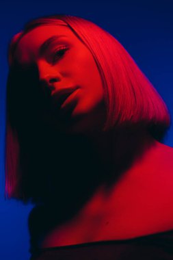 Derin mavi ve kırmızı ışık harmanlanmış, gizem ve cazibeyi çağrıştıran bir kadın yüzü.