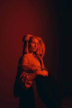 Kırmızı bir parıltıyla poz veren modacı kadın, sanatsal ifadesi modern bir stüdyo ortamında çekildi.