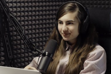 Sıcak bir gülümsemesi olan genç bir kadın podcast 'ini sunuyor, ses yalıtımlı bir stüdyoda profesyonel bir mikrofona konuşuyor.