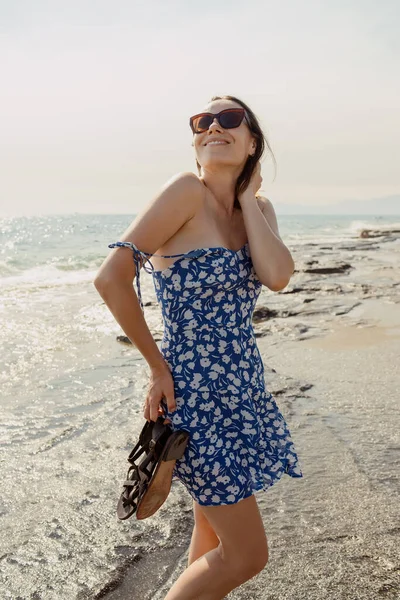 ビーチデーの輝きを捉え 風味豊かなドレスとサングラスの女性が海の呼びかけを感じる — ストック写真