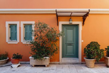 Yeşil kepenkleri ve saksısı olan bir Akdeniz evinin sıcak cephesi davetkar bir giriş yaratır.
