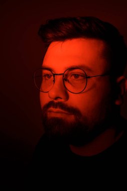 Derin düşüncelere dalmış bir adam, yüzü koyu kırmızı bir ışıkta yıkanmış, iç gözlem havası yaratıyor.