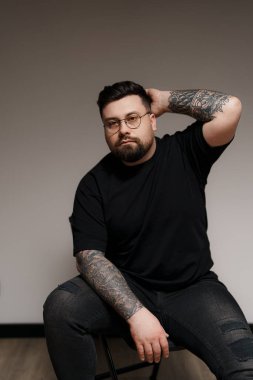 Detaylı kollu dövmeleri olan sıradan, soğukkanlı bir adam derin derin düşünür, kendinden emin bir şekilde oturur.