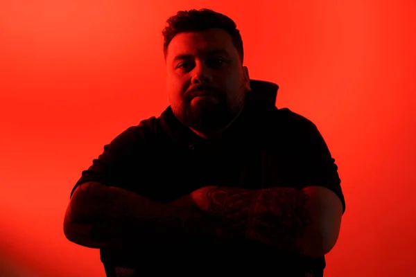 Silhouetted man with arms crossed and tattoos, exuding confidence on a vibrant red background
