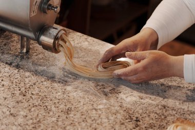 Anonim kadın aşçı mutfakta mermer tezgahta geleneksel İtalyan rulo taze tagliatelle makarna hazırlıyor.