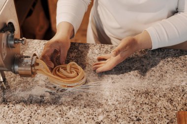 Anonim kadın aşçı mutfakta mermer tezgahta geleneksel İtalyan rulo taze tagliatelle makarna hazırlıyor.