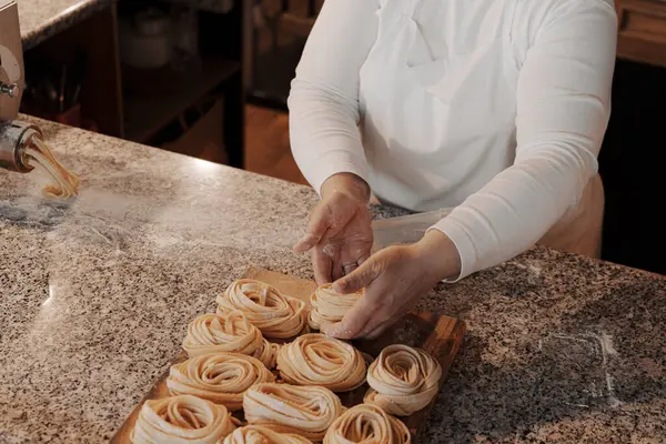 Yüksek açılı, isimsiz kadın aşçı. Mutfakta yemek hazırlarken, ahşap kesme tahtasına el yapımı rulo tagliatelle makarna koymuş.