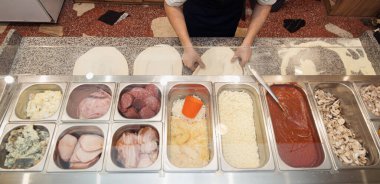 İşteki bir şefin tezgahta hazır bir dizi taze malzemeyle pizza hamuru uzatması.