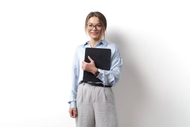 Gülümseyen genç bir profesyonel, iş kıyafeti giymiş, gözlüklü, temiz bir arkaplanı olan bir planlayıcıyı tutuyor.