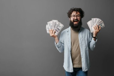 Sakallı ışıldayan adam gururla dolarların hayranlarını tutuyor, finansal başarı sergiliyor.