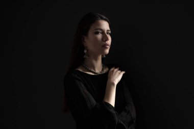 Siyah elbiseli bir kadın karanlık bir ortamda tek başına duruyor..