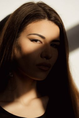 Görüntü, genç bir kadının yüzünü kısmen güneş ışığıyla aydınlatarak gölgelerle çarpıcı bir kontrast oluşturuyor..