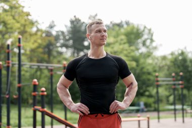 Siyah tişörtlü bir atlet derin bir duraksama yapar, elleri kalçada, gözleri gelecekteki hedeflerde titiz bir idman sırasında.