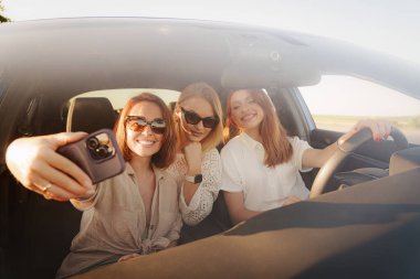 Üç kadın heyecanlı bir şekilde arabada bir özçekim için poz veriyor, arkadaşlıklarının neşesini yakalıyor ve kalıcı anılar yaratıyorlar..