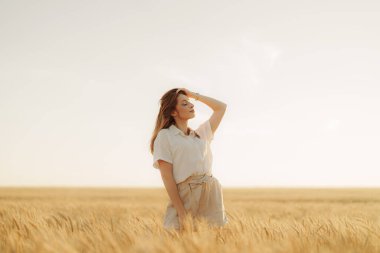 Batan güneşin sıcacık kucağında, bir kadın buğday tarlasında yalnız duruyor, düşüncelere dalmış ve anın güzelliği içinde kaybolmuş.