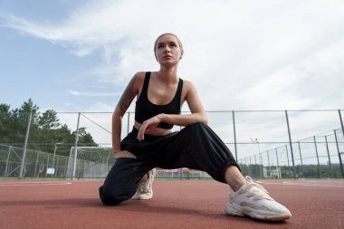 Spor meraklısı, güneşli bir spor sahasında egzersiz öncesi rutin hareketlerini sergiliyor.