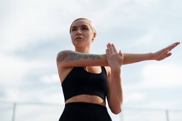 Любитель фитнеса занимается растяжками рук, фокусируясь на тренировках на облачном небе.