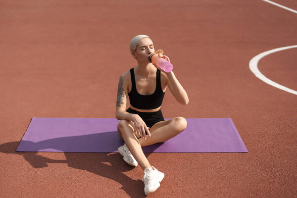 Любители фитнеса гидратируют, сидя на коврике для йоги на спортивном корте, подчеркивая здоровье