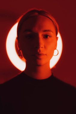 Bir kadının büyüleyici yakın çekimi, dairesel kırmızı neon ışıkla vurgulanarak bir halo etkisi yaratır.